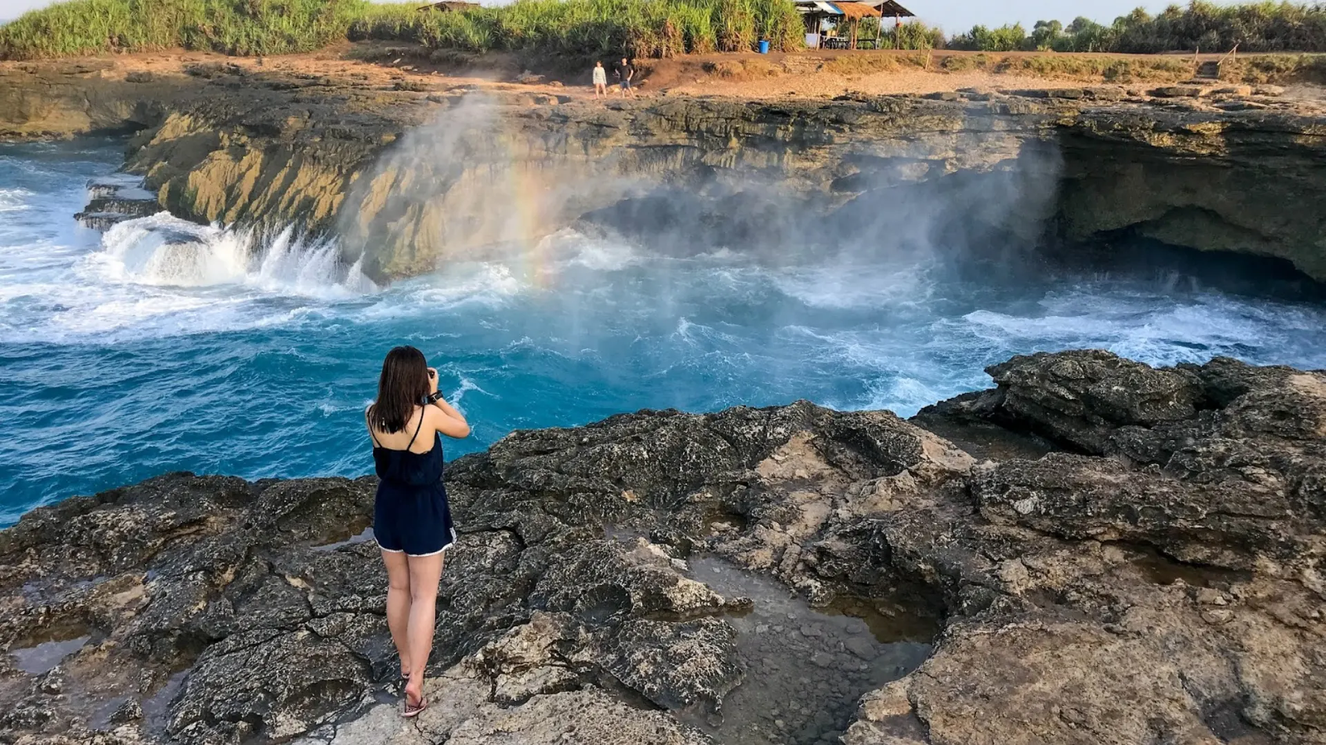 Tourist standing on the rocky edge capturing the dramatic ocean spray at Devil's Tears Nusa Lembongan.