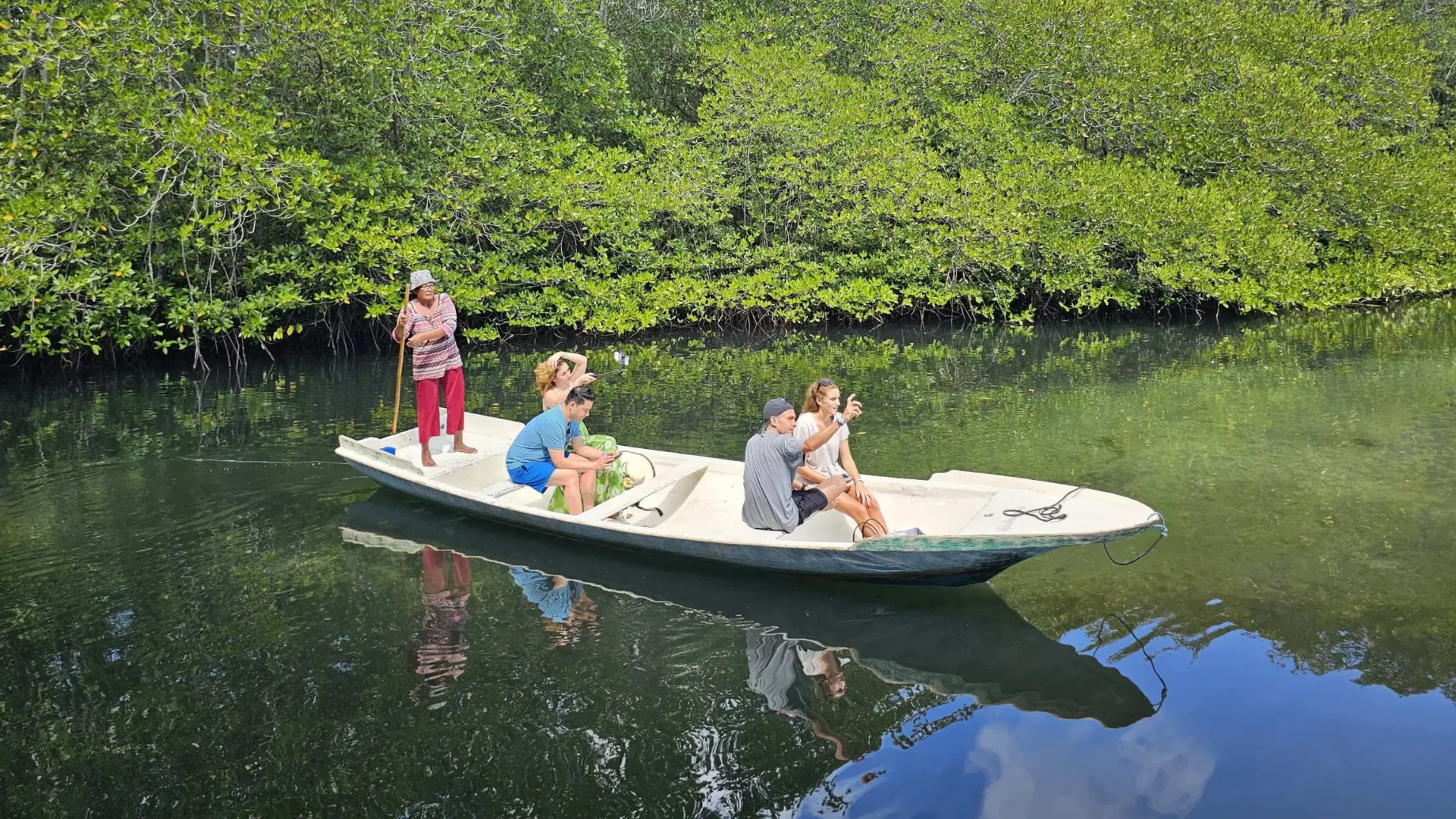 Tourists enjoying a traditional outrigger boat tour inside the serene, shaded rivers of Mangrove Forest Nusa Lembongan.