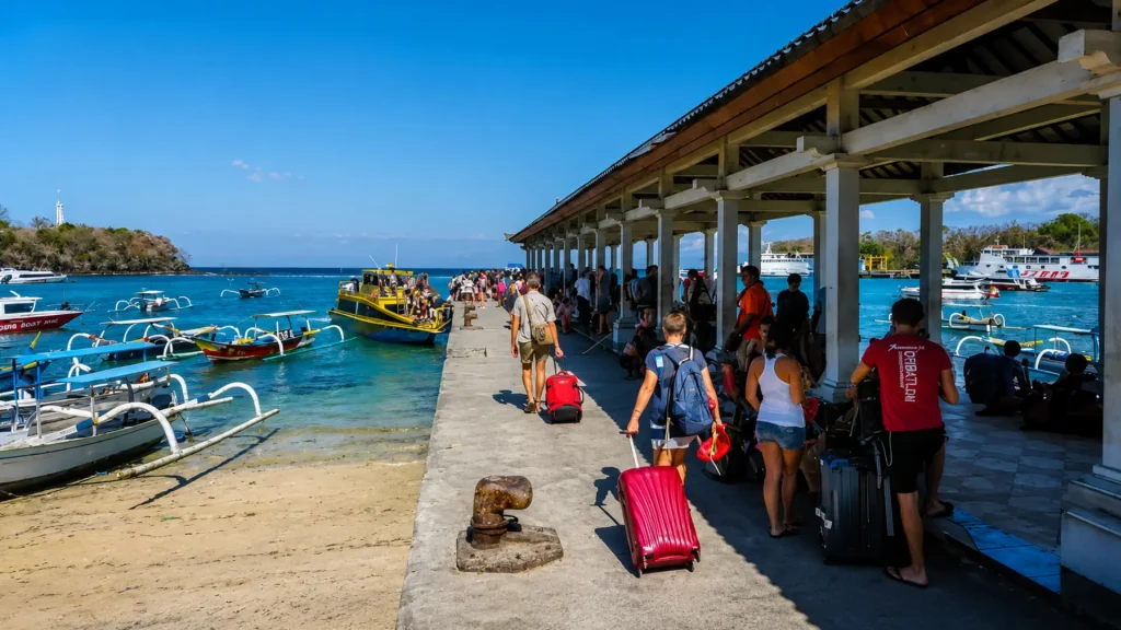 Travelers carrying suitcases along the sheltered concrete pier toward the speedboats in the Padang Bai port travel guide.