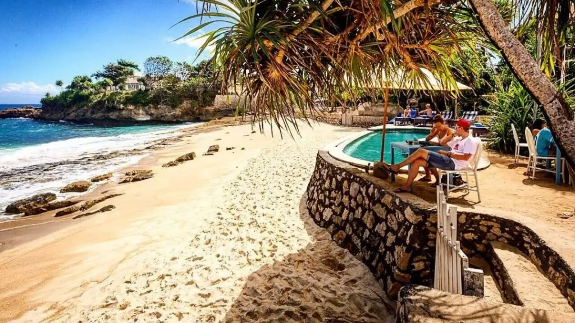 Luxury infinity pool and beachfront lounge chairs at Sandy Bay Beach Club Nusa Lembongan during sunset.